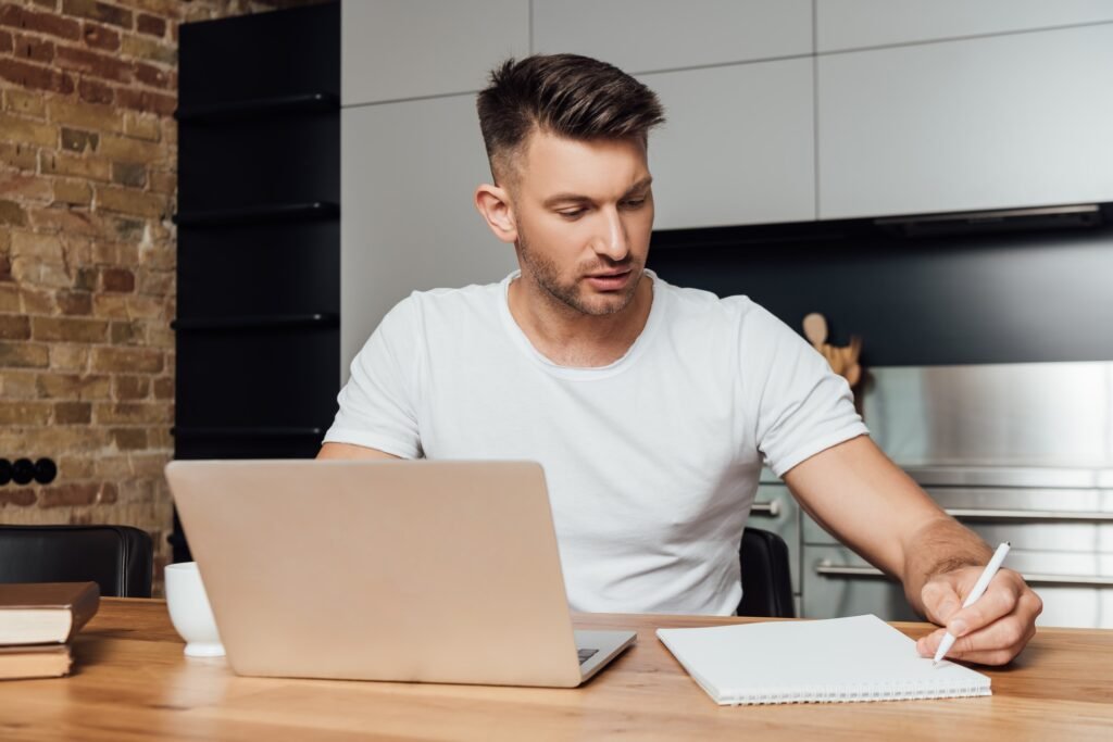 handsome man holding pen near notebook and laptop while online study